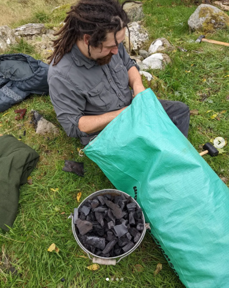 Andrew packing charcoal by hand, with a bucket of lumpwood beside him